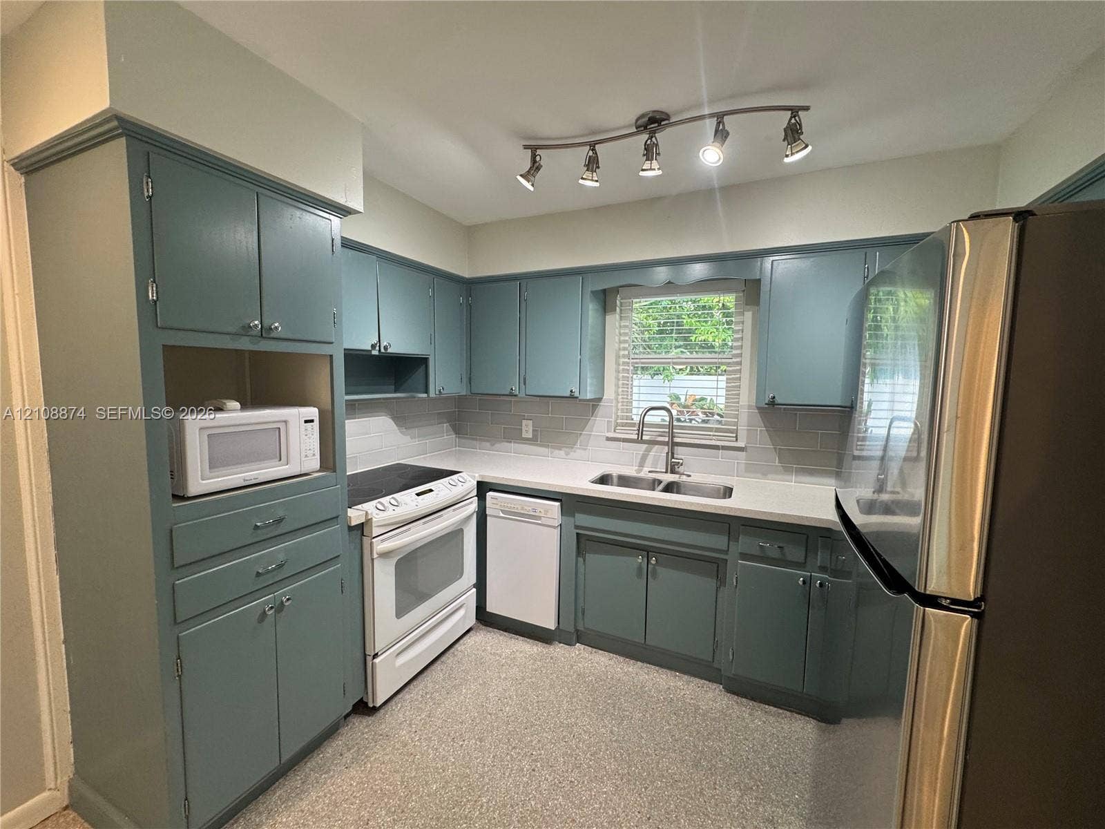Kitchen featuring painted cabinetry, subway tile backsplash, solid surface countertops, dual-basin stainless steel sink with pull-down faucet, and adjustable multi-light track lighting