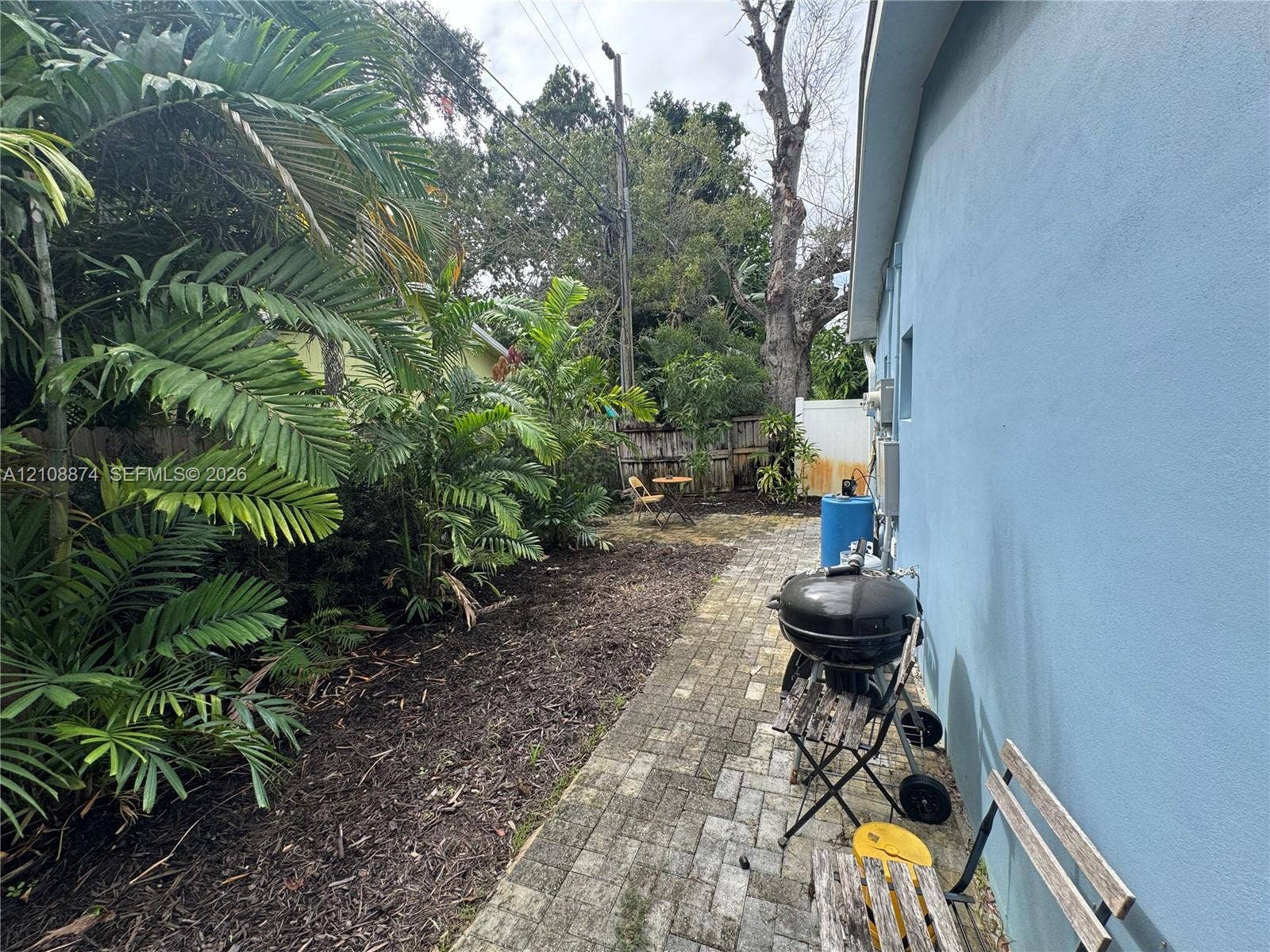 Side yard featuring a paved brick walkway, mature palm landscaping, and wood-panel fencing