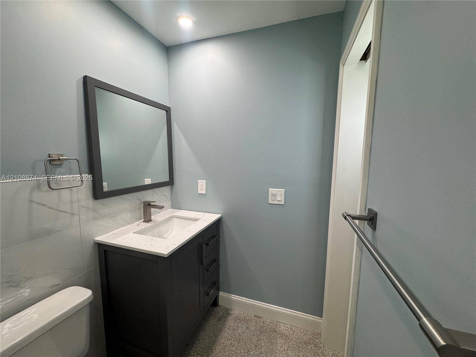 Vanity with a solid surface countertop, undermount sink, dark-finish cabinetry, framed wall mirror, and metal wall-mounted hardware