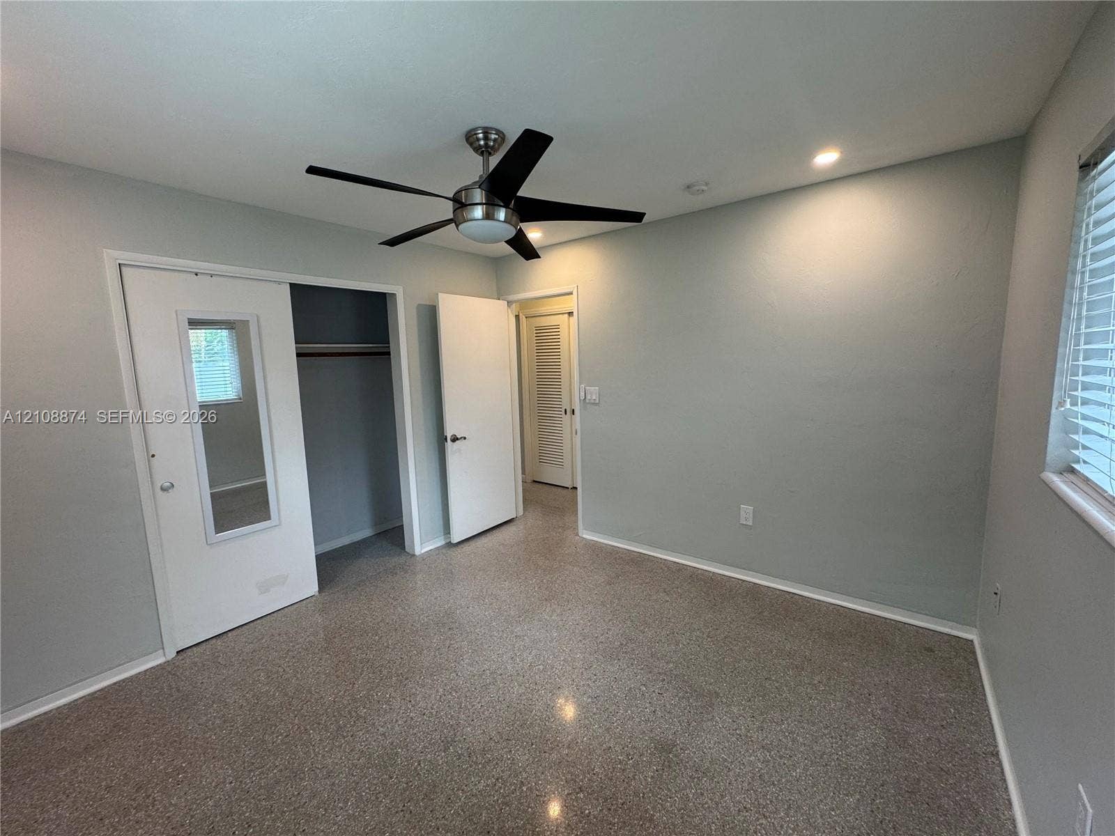 Neutral-toned interior featuring terrazzo flooring, a multi-blade ceiling fan with integrated lighting, recessed ceiling lights, and a closet with a mirrored door panel