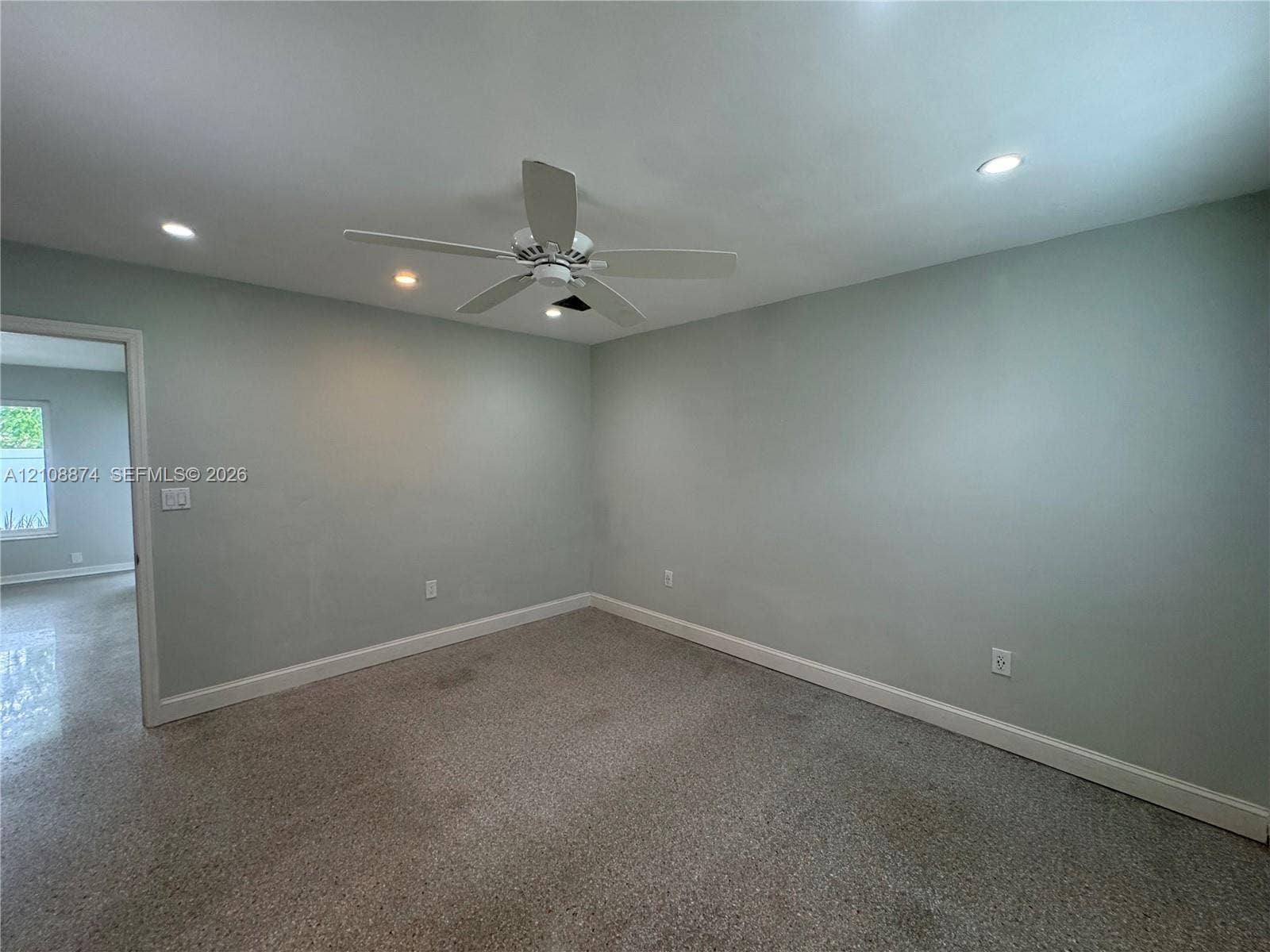 Neutral-toned interior space featuring recessed ceiling lighting, a central white ceiling fan, and carpeted flooring