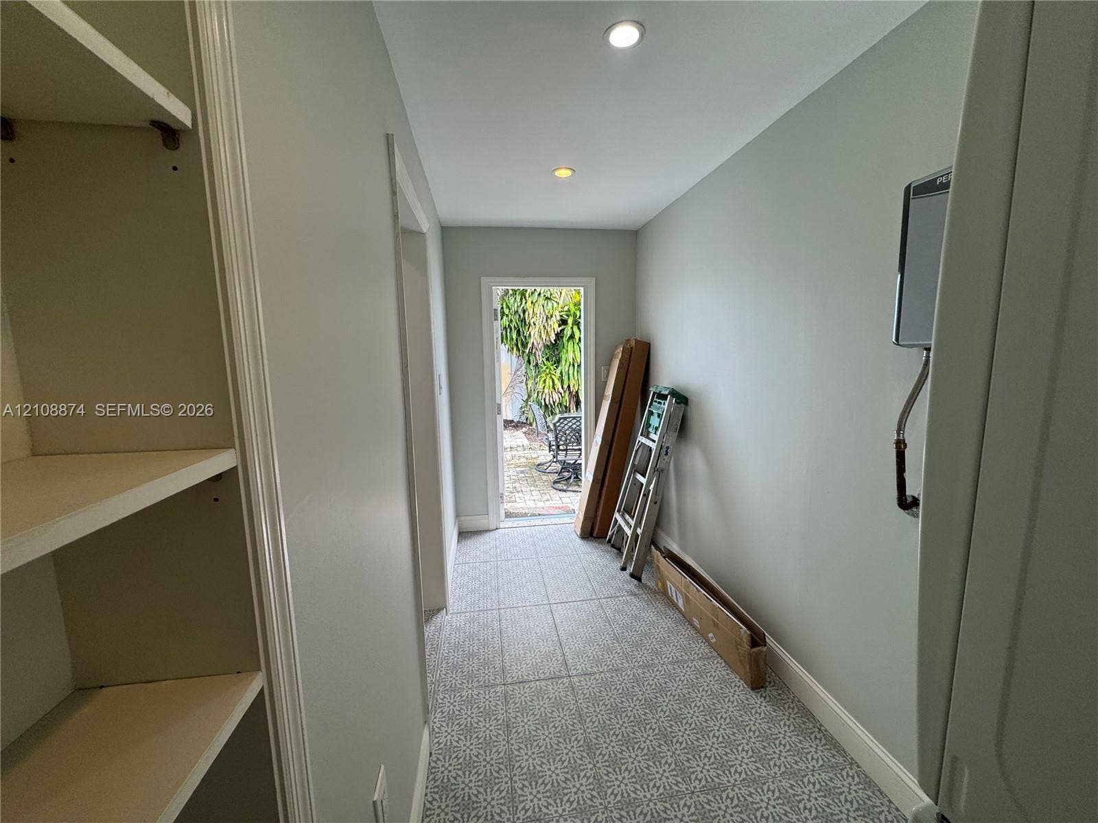 Hallway featuring patterned tile flooring, built-in shelving, recessed ceiling lighting, and a doorway providing egress to the exterior