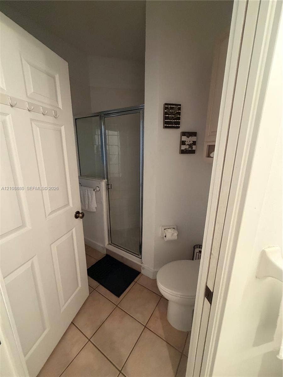 Bathroom featuring a tiled floor, a glass-enclosed shower stall, and a porcelain toilet