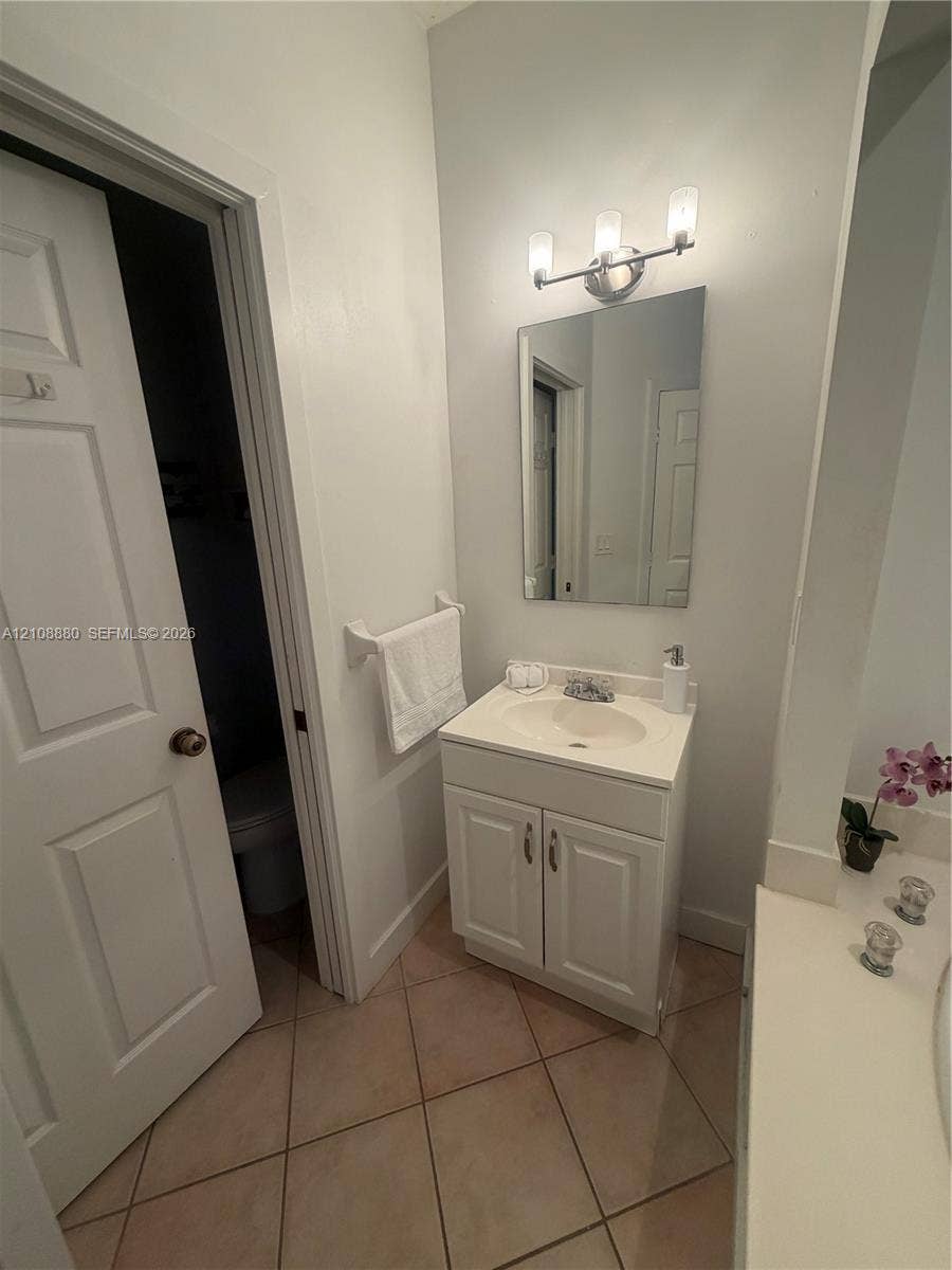 White vanity cabinet with an integrated sink basin, wall-mounted three-light fixture, rectangular frameless mirror, and neutral tile flooring