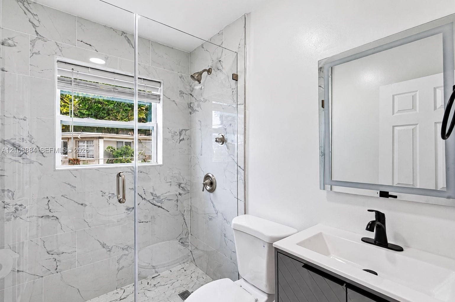 Walk-in shower enclosure with vein-patterned wall tile, vanity with a rectangular basin and matte black faucet, and a wall-mounted lighted mirror