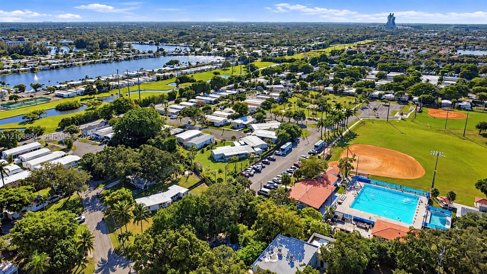 Aerial perspective of the community featuring a swimming pool, baseball diamond, paved parking area, and canal-front scenery
