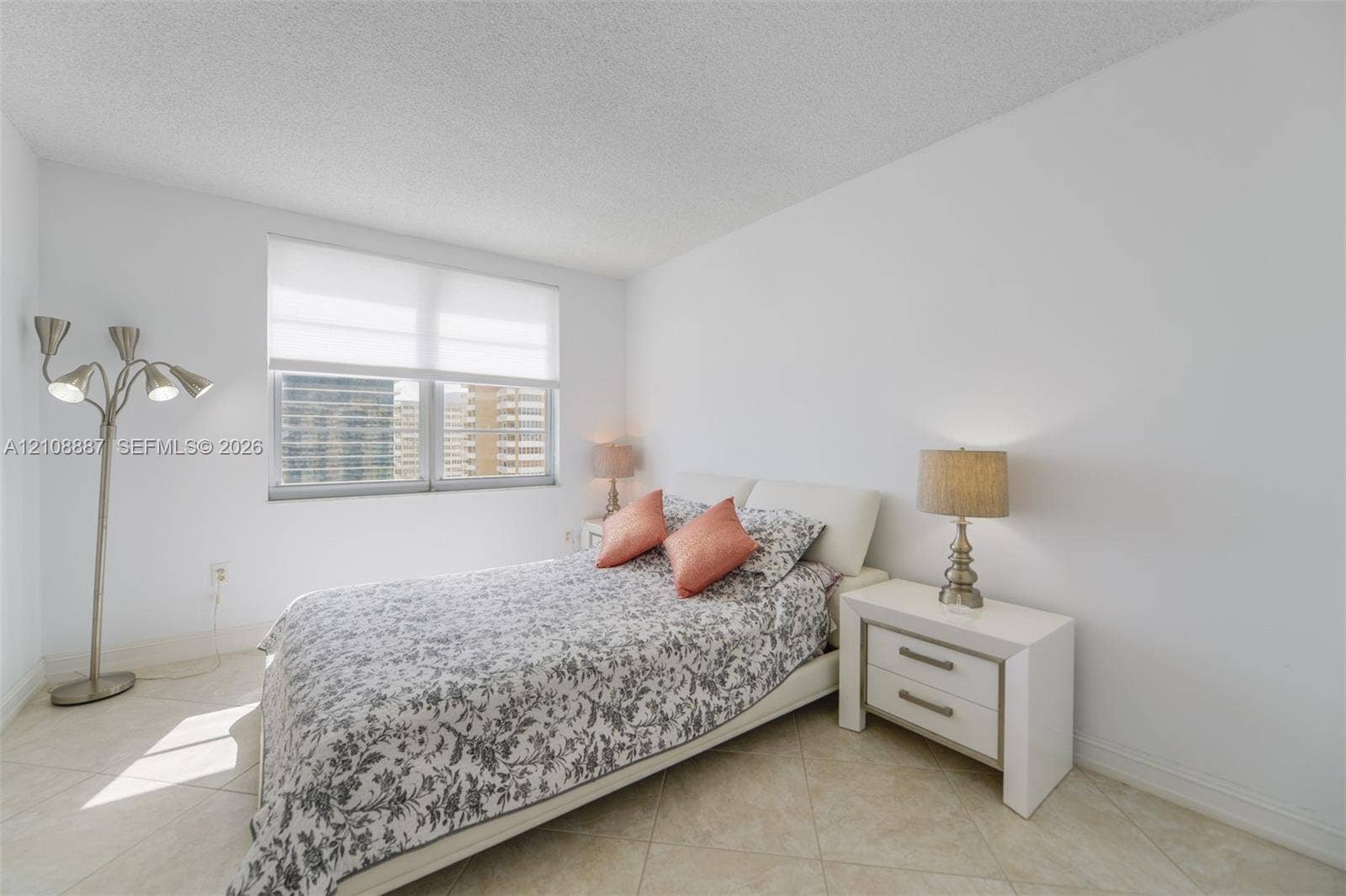 Neutral interior space featuring polished tile flooring, white walls, and a large window with white roller shades