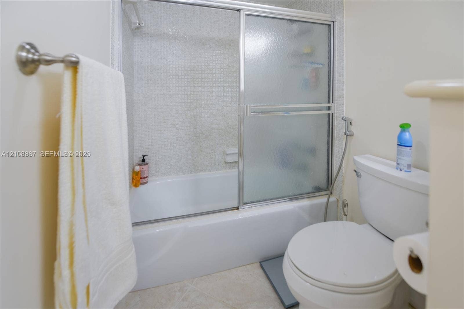 Bathroom featuring a combination bathtub and shower with a glass sliding enclosure, mosaic tile surround, and a wall-mounted towel bar
