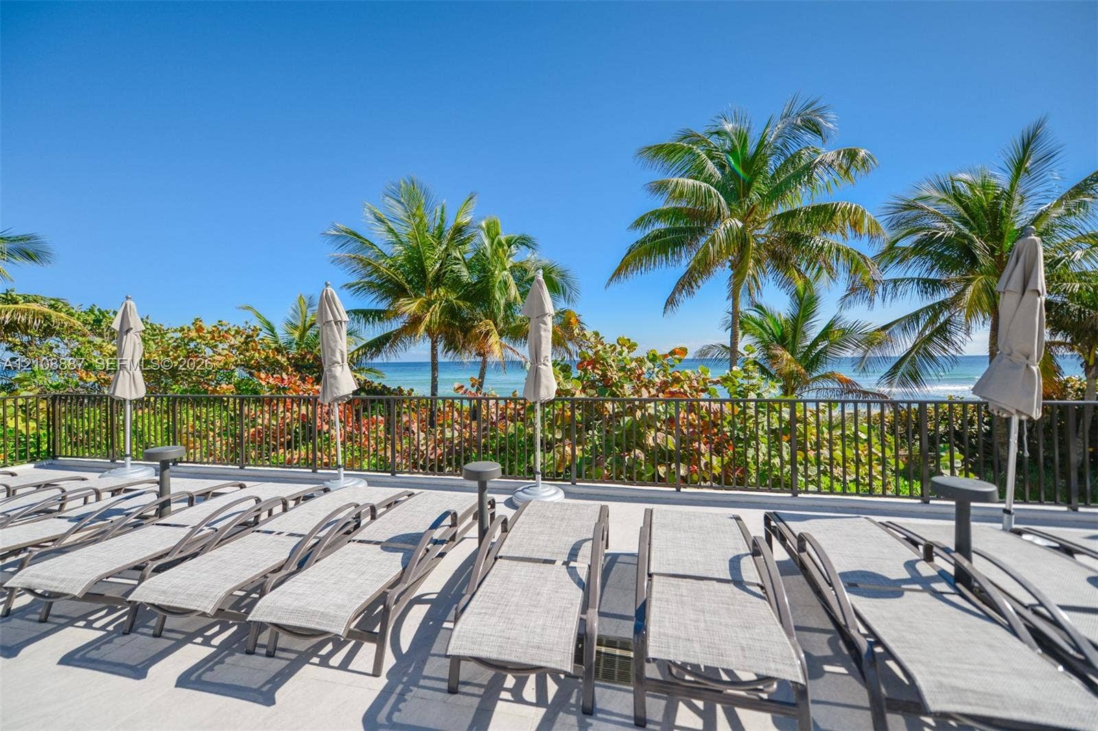 Elevated outdoor deck featuring hard surface flooring, metal safety railing, and tropical landscaping with ocean backdrop