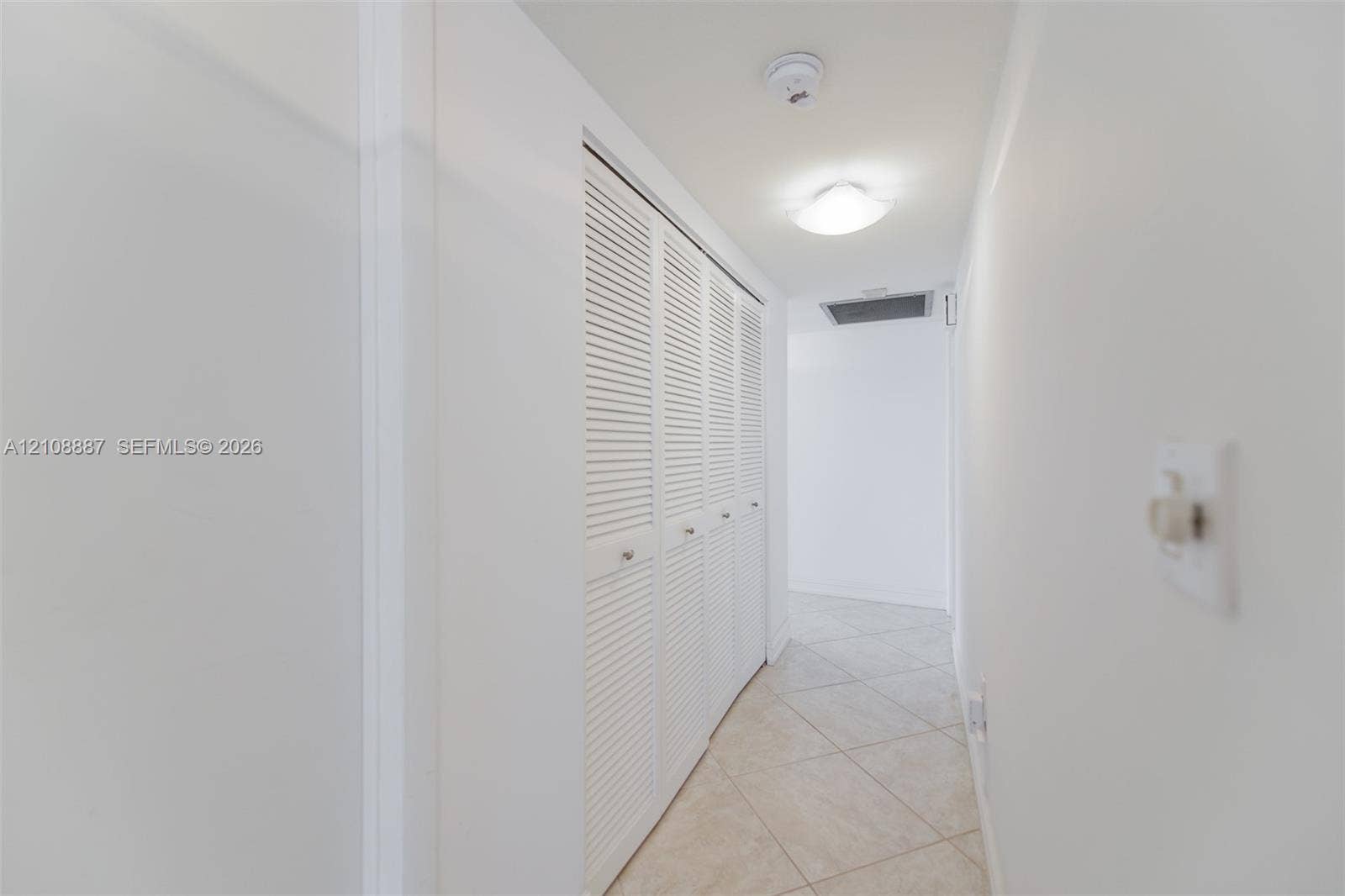 Hallway featuring neutral-toned tile flooring and white bi-fold louvered closet doors