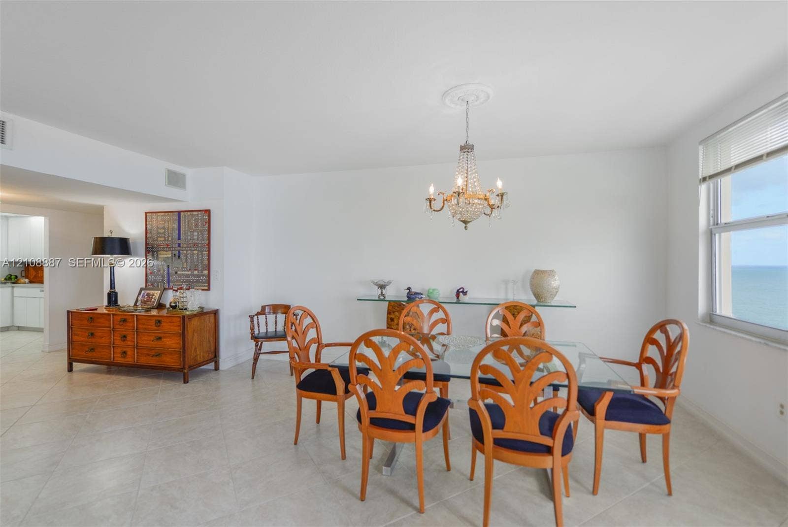 Open-concept living space featuring large-format tile flooring, a decorative crystal chandelier with ceiling medallion, and oversized windows providing an expansive water horizon