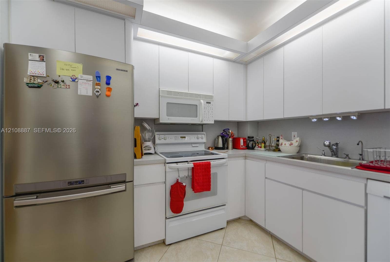 Kitchen featuring floor-to-ceiling white cabinetry, integrated recessed lighting, stainless steel refrigerator, white electric range with over-the-range microwave, and tile flooring