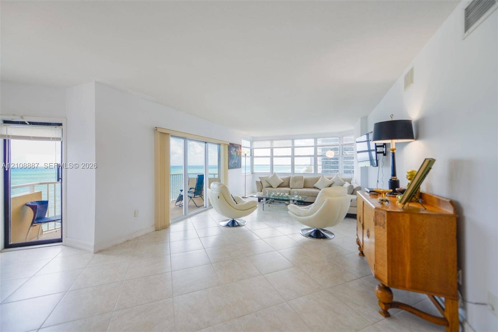Living area featuring large-format ceramic tile flooring, floor-to-ceiling windows, and access to a balcony with ocean scenery