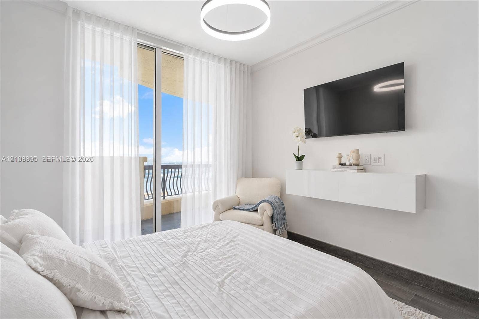 Floor-to-ceiling glass sliding doors opening to a balcony, wall-mounted white floating console, dark wood-finish flooring, and circular LED pendant lighting