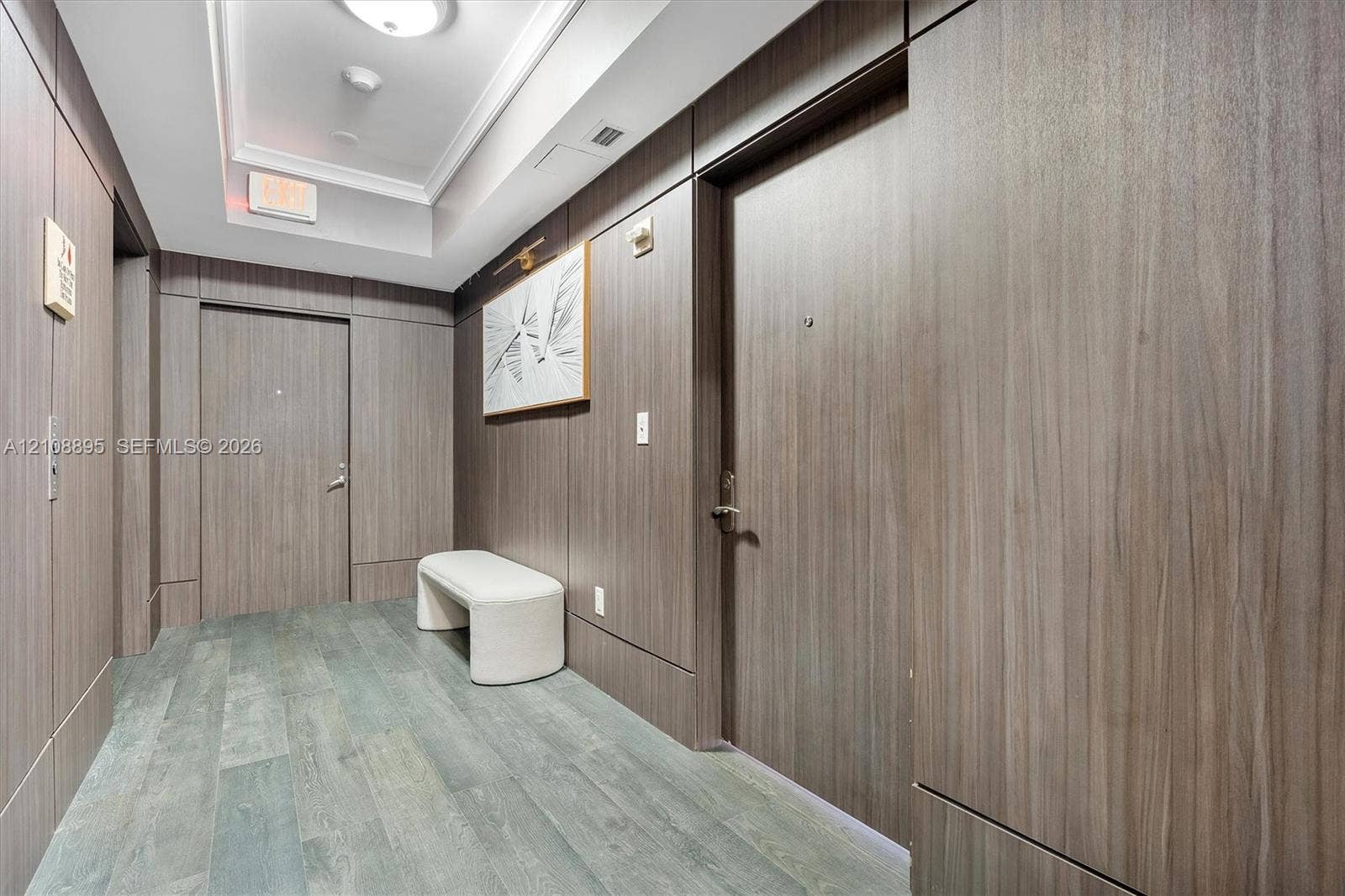 Hallway featuring wood-finish wall paneling, flush-mount lighting, tray ceiling, and wood-finish flooring