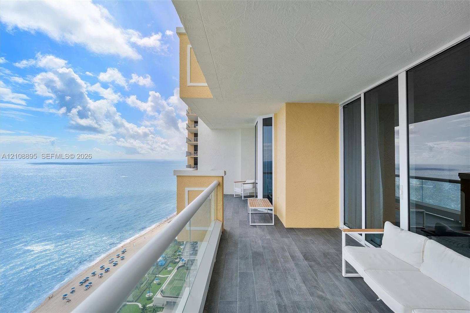 Covered balcony featuring wood-finish tile flooring, glass panel railings, and floor-to-ceiling windows