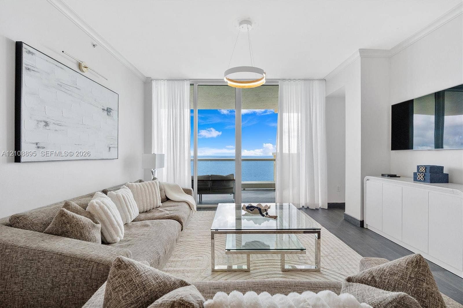 Living space featuring floor-to-ceiling glass sliding doors, dark wood-finish flooring, built-in cabinetry, circular pendant lighting, and an expansive balcony