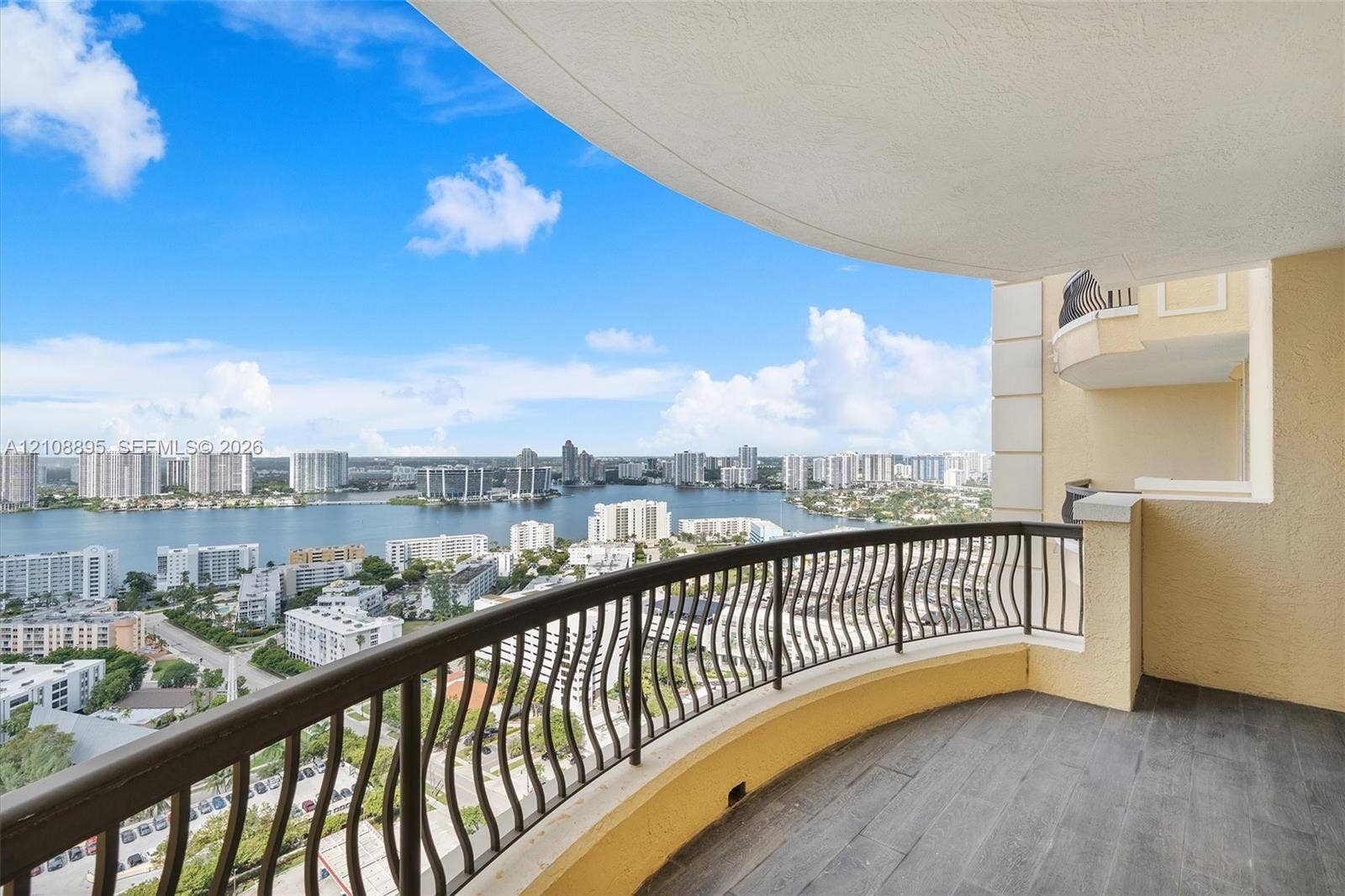 Covered private balcony featuring dark tile flooring, arched structural design, and metal decorative railings