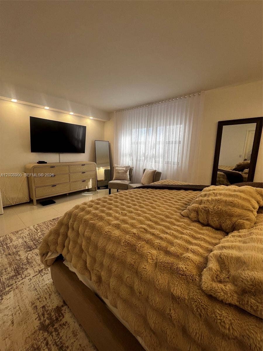 Recessed lighting, light-toned tile flooring, and a window treatment spanning the width of the wall