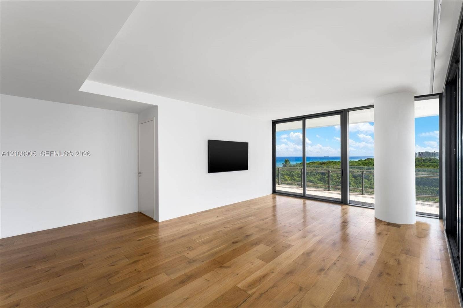 Interior space featuring wood-finish flooring, floor-to-ceiling sliding glass doors, a structural support column, and a balcony with an ocean backdrop