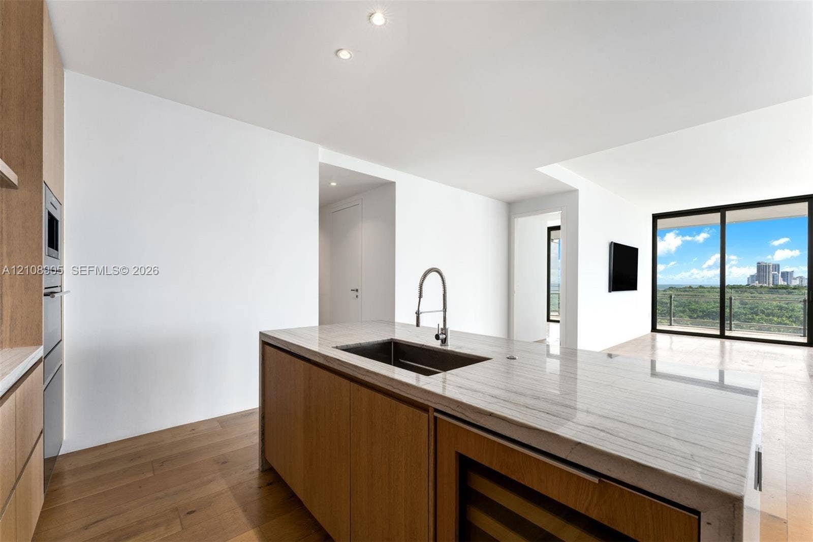 Modern kitchen featuring an island with stone countertops, undermount sink, built-in wine refrigeration, and wood-finish cabinetry