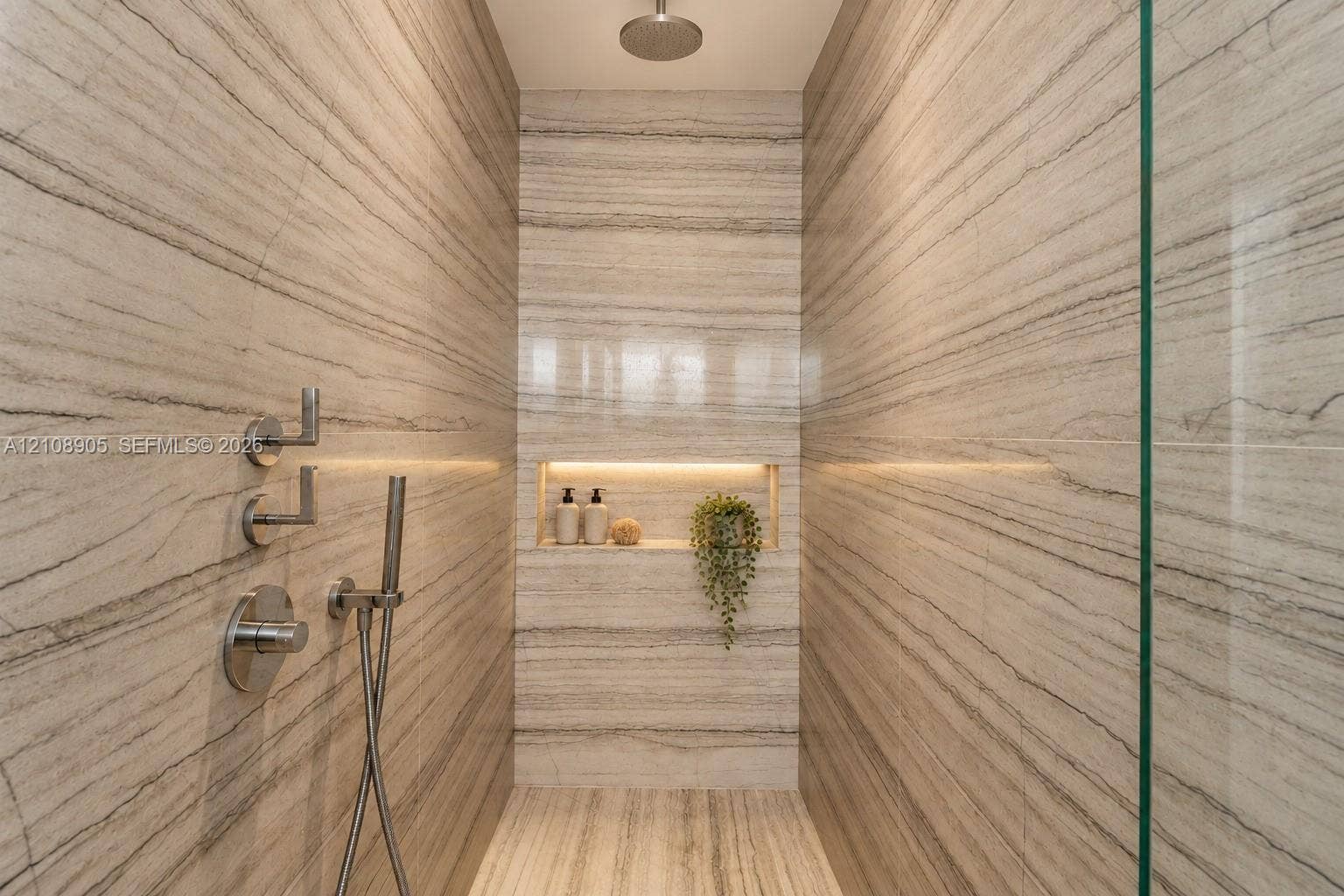 Walk-in shower featuring full-height linear vein stone wall tiling, a rainfall showerhead, a separate handheld sprayer, a glass enclosure, and a recessed wall niche with integrated lighting