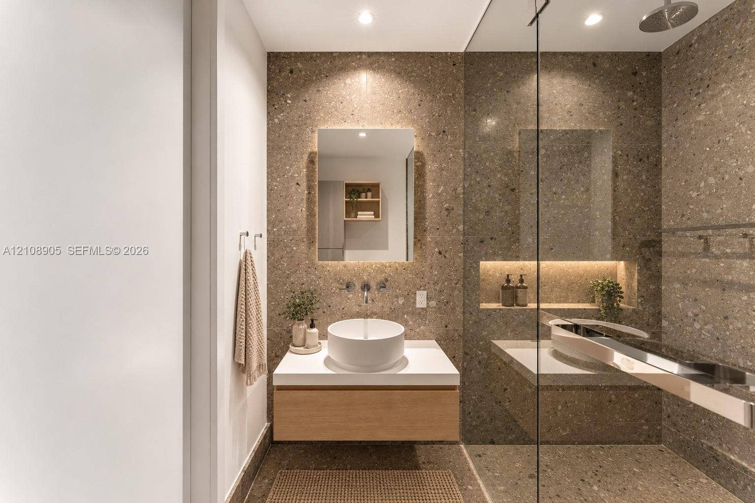 Floating wood-finish vanity with a white vessel sink, wall-mounted faucet, integrated recessed shelving with lighting, and floor-to-ceiling stone-composite wall cladding