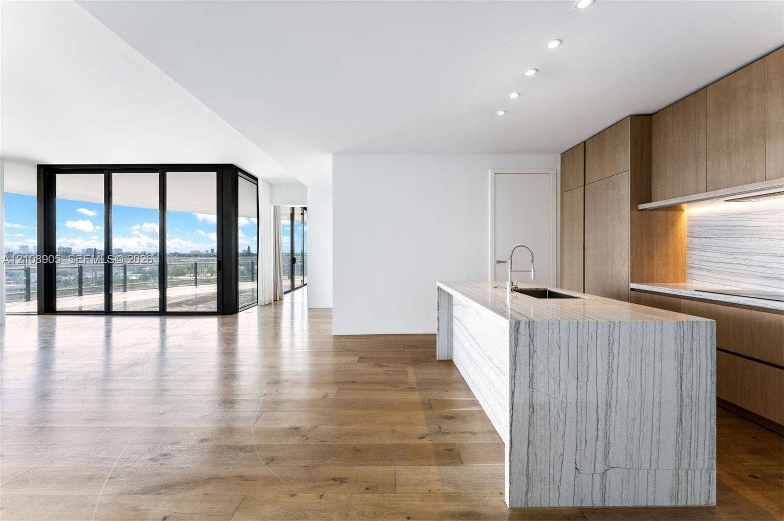 Modern kitchen featuring a waterfall-edge island, stone-surfaced countertops, wood-finish cabinetry, wood-finish flooring, and floor-to-ceiling glass wall systems