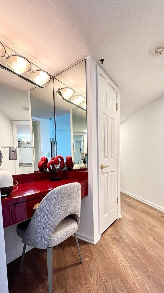 Built-in wall-mounted vanity with a high-gloss finish, expansive wall-to-wall mirror, multi-bulb overhead lighting, six-panel interior door, and wood-finish flooring