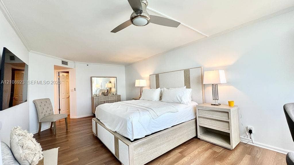 Room featuring wood-finish flooring, a contemporary brushed-metal ceiling fan with integrated lighting, and crown molding