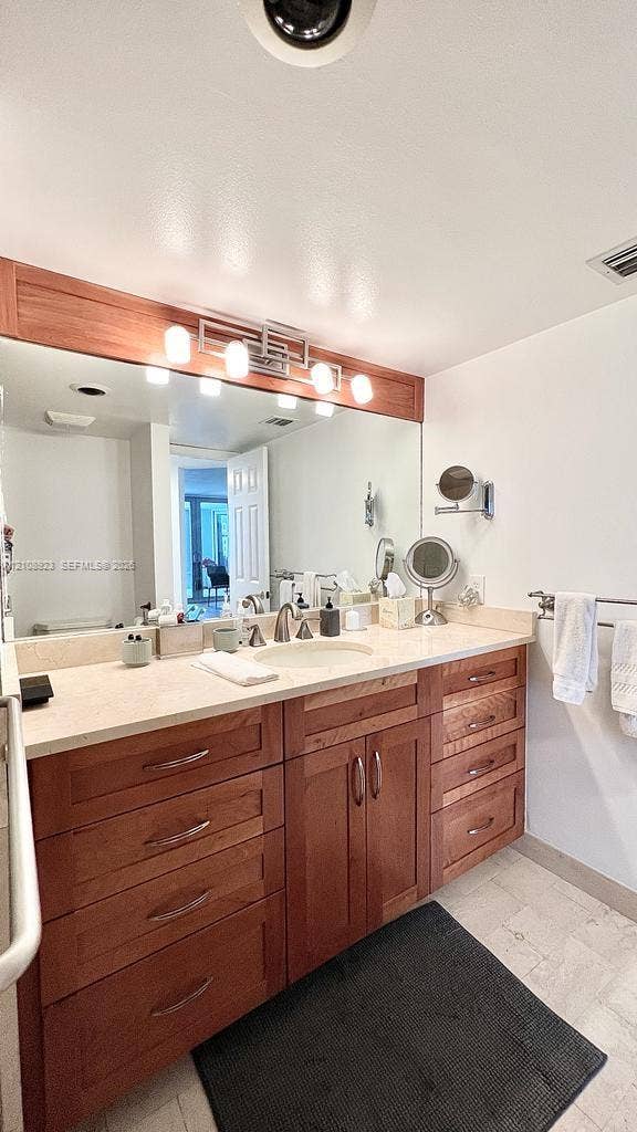 Wood-finish vanity cabinetry with multiple storage drawers, light-toned countertop featuring an integrated sink, expansive mirror, and a wall-mounted multi-bulb light fixture