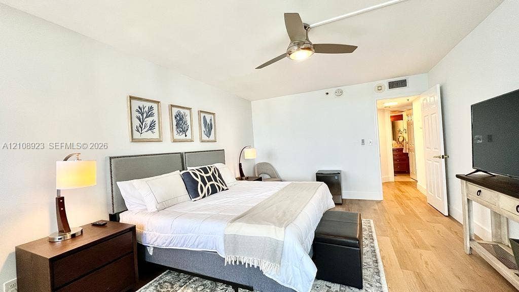 Wood-finish flooring, brushed metal ceiling fan with integrated lighting, and white paneled interior door