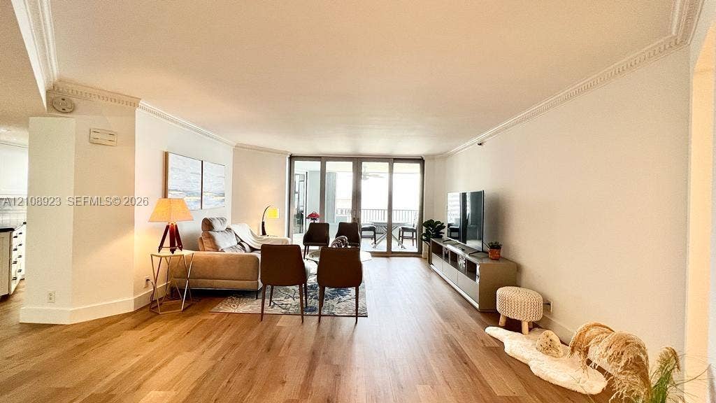 Open-concept room featuring wood-finish flooring, crown molding, and large sliding glass doors providing outdoor access