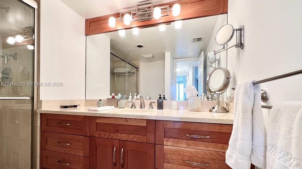 Bathroom vanity featuring solid wood cabinetry, a light-toned stone countertop, integrated sink, and an expansive wall-mounted mirror with integrated lighting