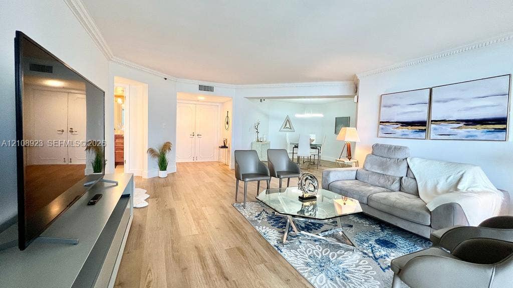 Open-concept interior featuring light wood-finish flooring, crown molding, and double-door entryway