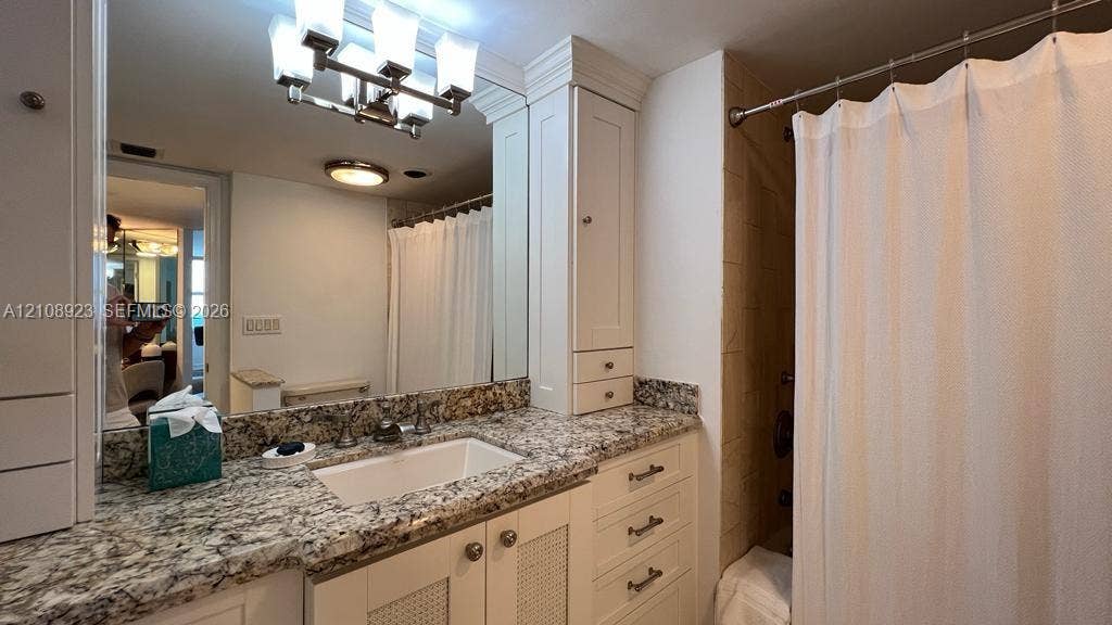 Bathroom featuring a vanity with stone-finish countertop, white cabinetry with integrated storage, rectangular undermount sink, and multi-bulb light fixture