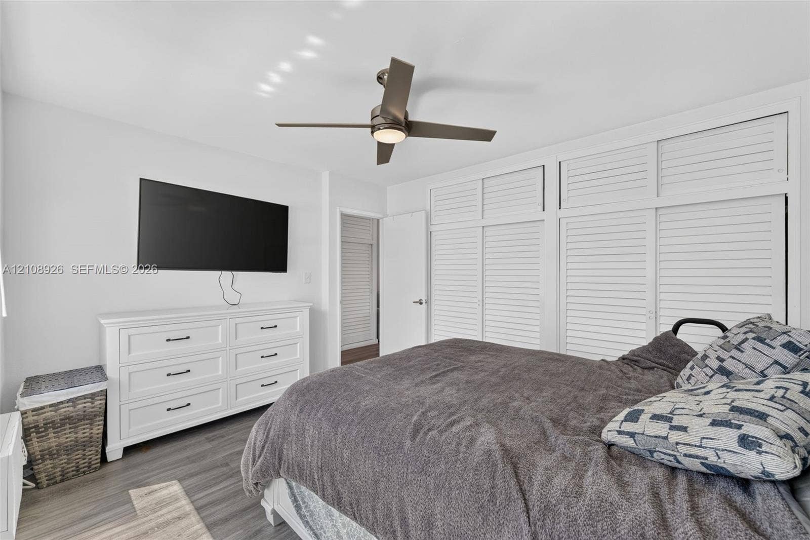 Bedroom featuring wood-finish flooring, floor-to-ceiling built-in white louvered-style cabinetry, and a central ceiling fan with integrated lighting