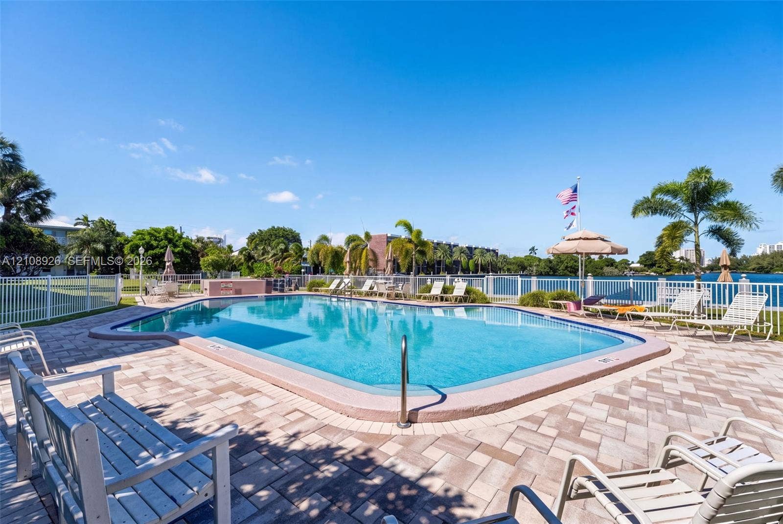 In-ground pool featuring a perimeter fence, stone-paver decking, and a metal ladder entry
