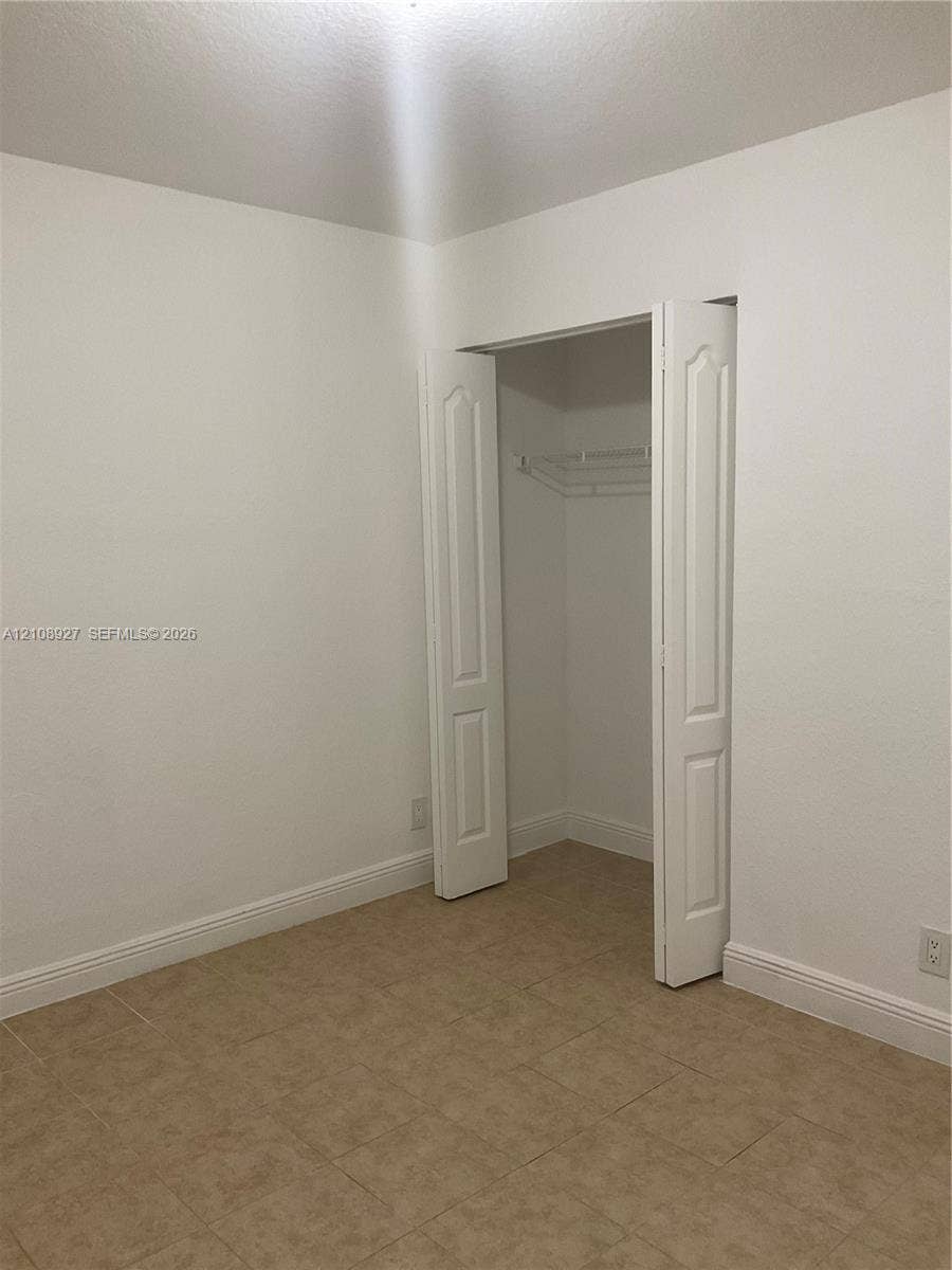 Room featuring neutral wall finishes, tile flooring, and a closet with bifold doors and built-in wire shelving