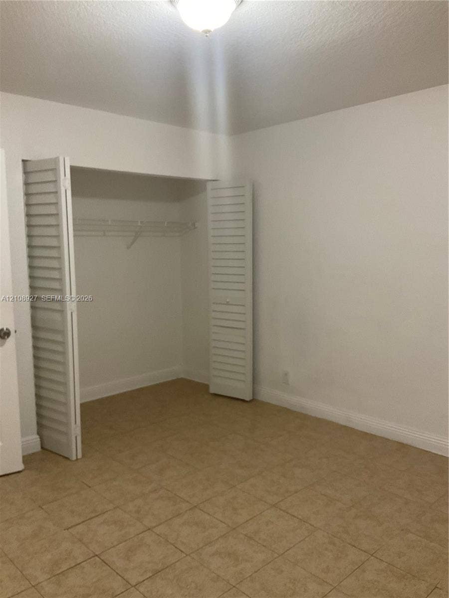 Room featuring tile flooring, a closet with white louvered bi-fold doors, and a ceiling-mounted light fixture