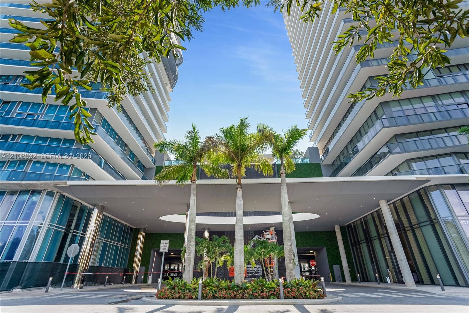 1170 E Hallandale Beach Boulevard, #1201, Hallandale Beach, FL 33009 Contemporary high-rise architecture featuring glass facade paneling, covered porte-cochre, recessed lighting, and integrated landscaping with mature palm trees