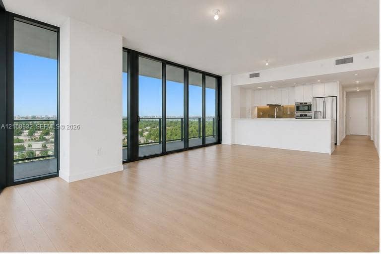 1170 E Hallandale Beach Boulevard, #1201, Hallandale Beach, FL 33009 Open-concept living space featuring floor-to-ceiling windows with dark frames, wood-finish flooring, and a kitchen equipped with white flat-panel cabinetry and stainless steel appliances