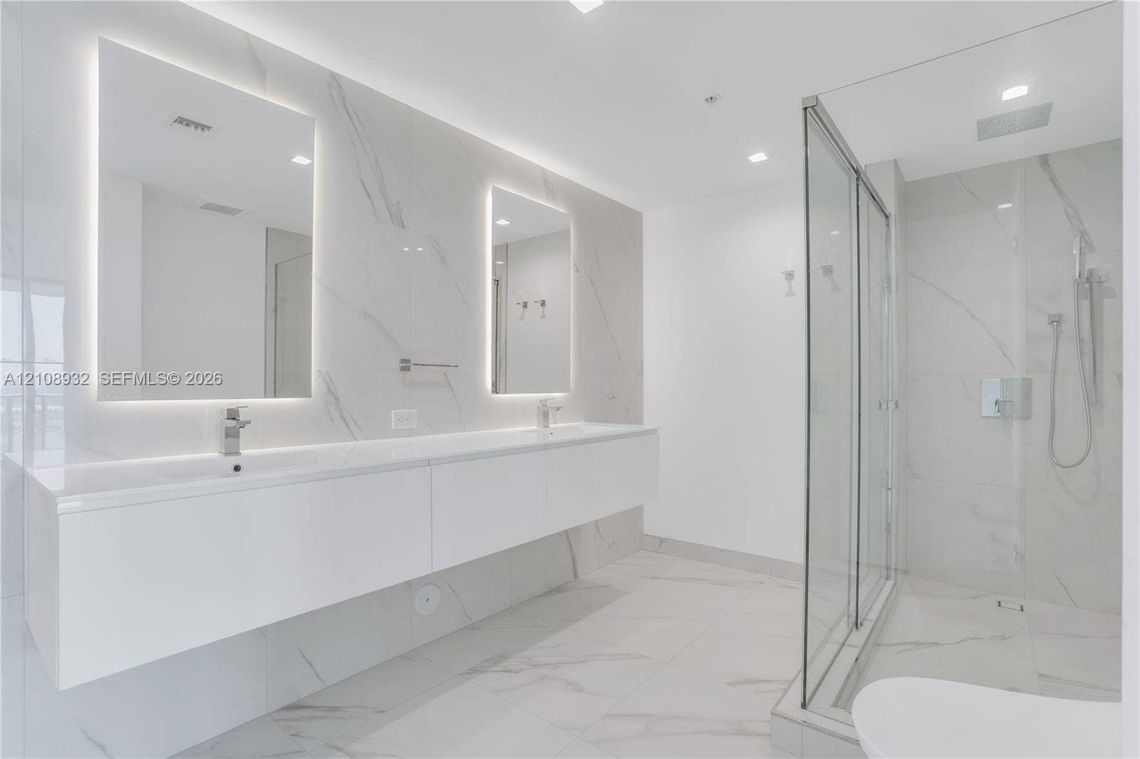 1170 E Hallandale Beach Boulevard, #1201, Hallandale Beach, FL 33009 Floating dual vanity with integrated sinks, back-lit mirrors, walk-in glass shower enclosure, and full-height stone-finish wall tiling