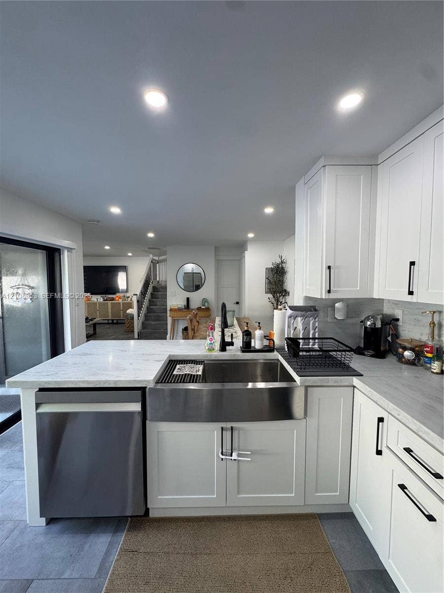 Kitchen featuring white shaker-style cabinetry, quartz countertops, a stainless steel apron-front sink with matte black hardware, integrated dishwasher, and recessed ceiling lighting