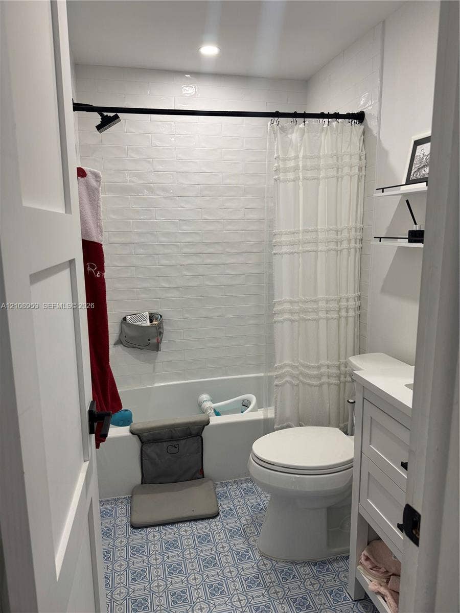 Bathroom featuring patterned floor tile, white subway tile shower surround, recessed ceiling lighting, a white vanity with integrated cabinetry, and matte black hardware