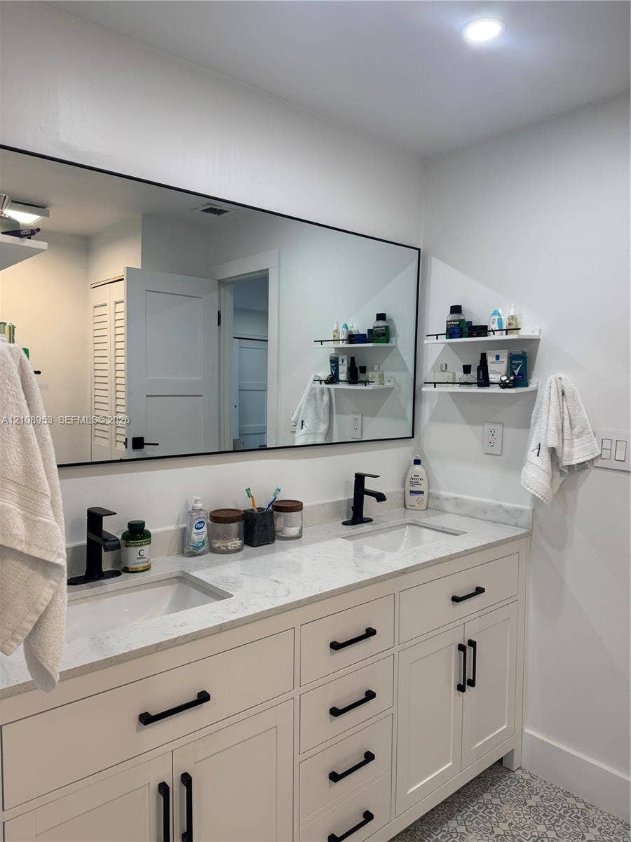 White double-sink vanity featuring a light-toned stone countertop, matte black hardware, integrated rectangular basins, and a large wall-mounted mirror