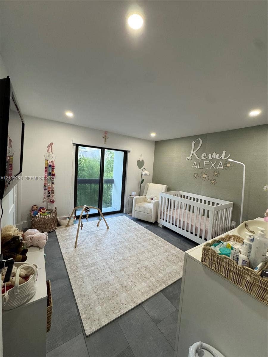 Neutral-toned interior space featuring large-format tile flooring, recessed ceiling lighting, a textured accent wall, and glass sliding doors with black framing