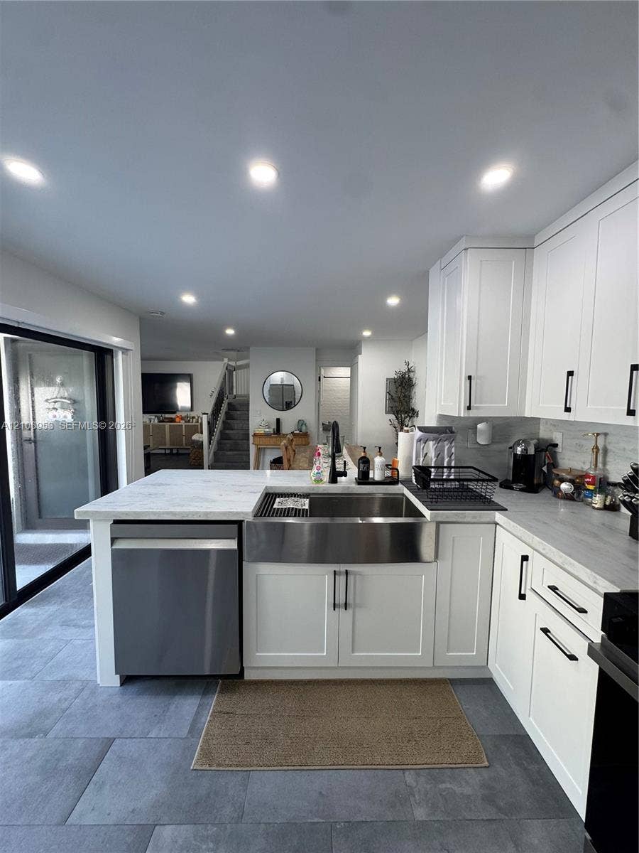 Kitchen featuring white shaker-style cabinetry, stainless steel apron-front sink, stone-finish countertops, recessed lighting, and large-format tile flooring