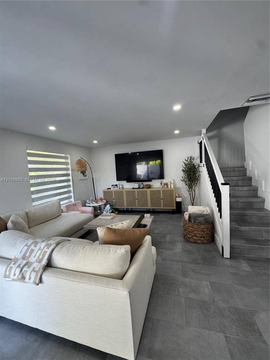 Large-format tile flooring, recessed lighting, and a staircase featuring a white handrail with black balusters