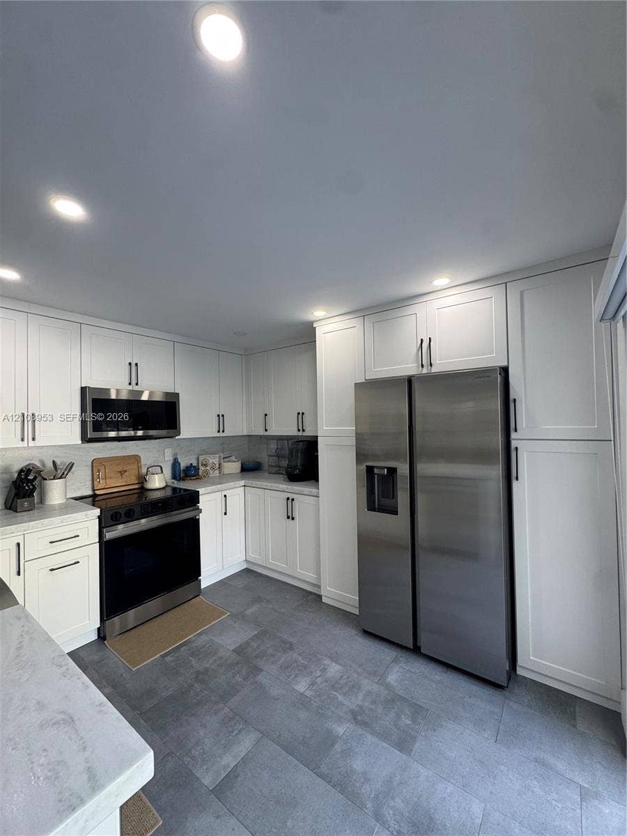 Kitchen featuring white shaker-style cabinetry, stainless steel appliances, stone-finish countertops, and large-format tile flooring